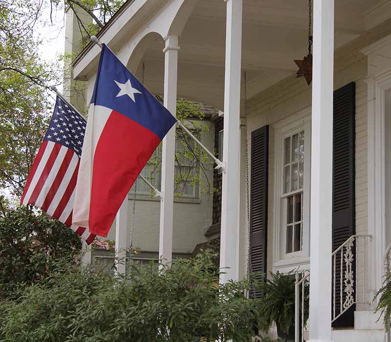 Close up of a large residential home with the American and Texas flag hanging on the front side