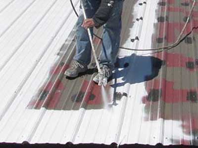 Close up of a worker spraying a white, waterproof coating on a metal commercial roof