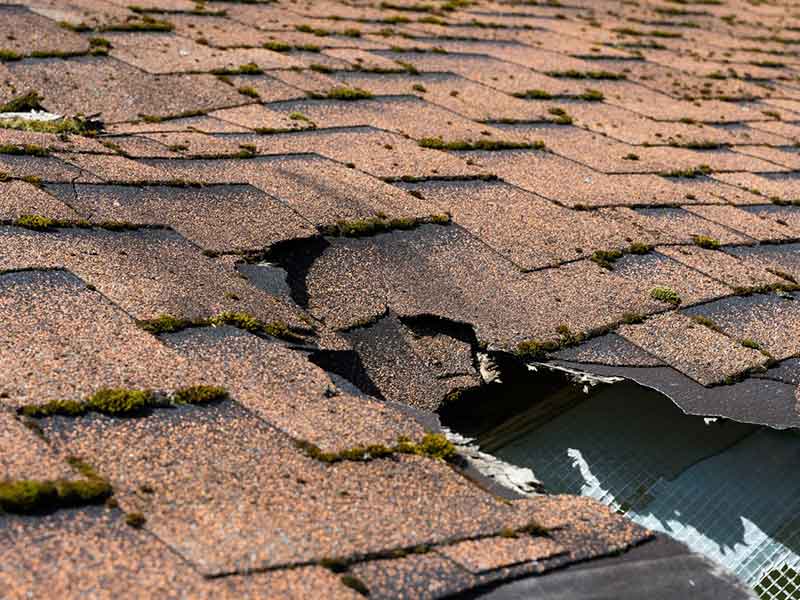 Close up of a large hole on a residential roof with brown shingles