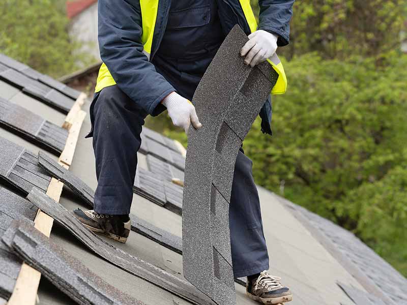 Worker on a residential roof holding and placing down asphalt shingles and getting them ready to be installed